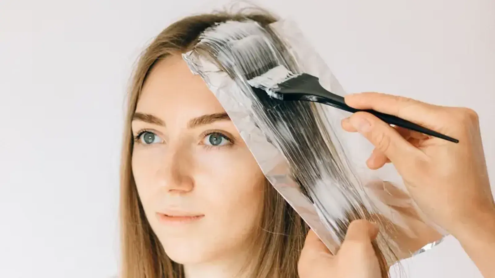A colorist brushing lightener onto a section of a woman's long hair laid over a sheet of foil