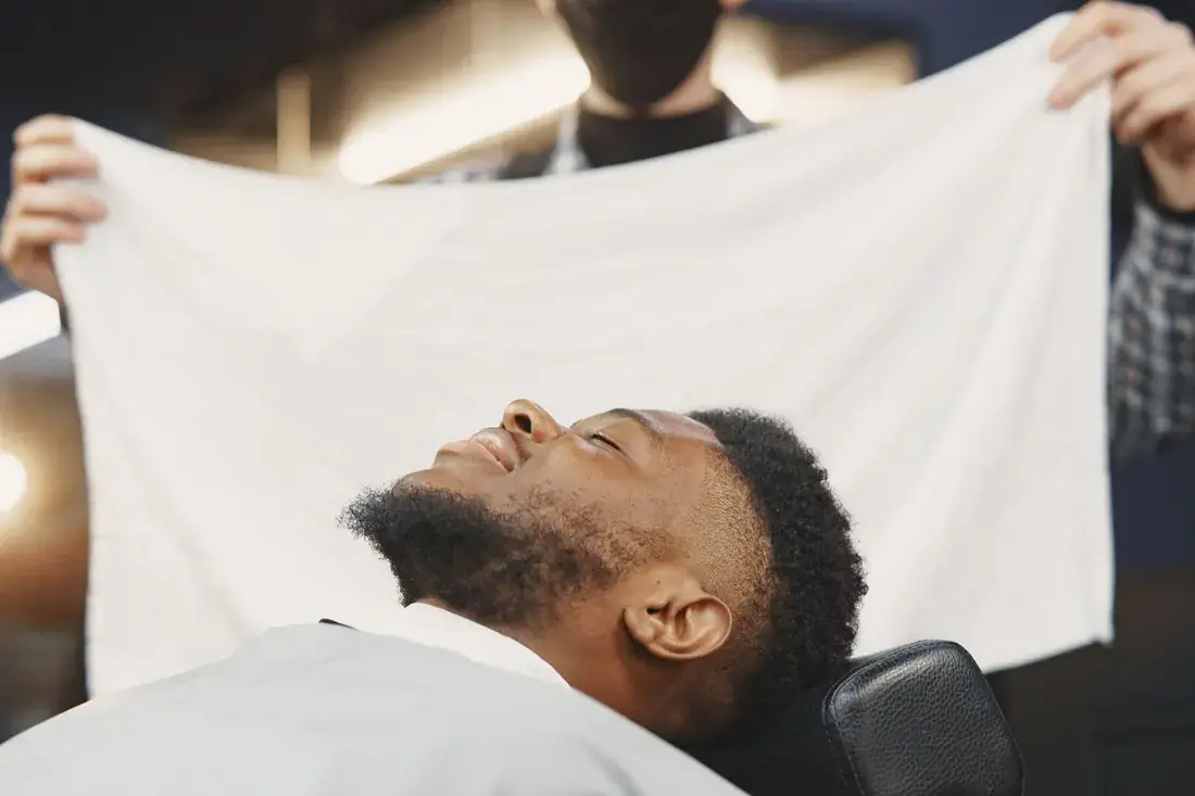A guest leaning back in the chair as a warm towel is placed over his face