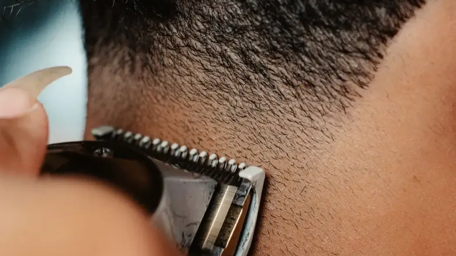 Close-up of clippers blending short hair down toward the skin at the back of a man's neck