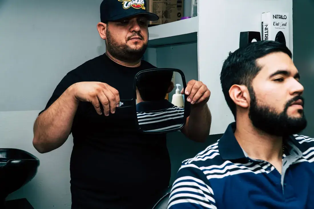 A barber holding a hand mirror so the guest can check his cut